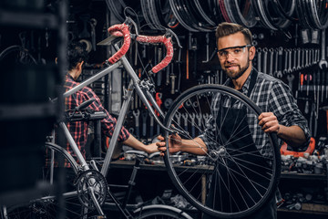 Wall Mural - Handsome smiling man in protective glasses is fixing bicycle at his own shop.