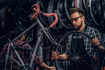 Wall Mural - Focused attractive man in glasses is chainging wheel for bicycle at busy workshop.