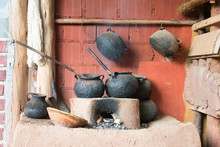 View Of A Lit Clay Oven And Some Slightly Worn Iron Pots On A Red Brick Wall