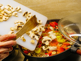 Adding mushrooms to pan vegetables.