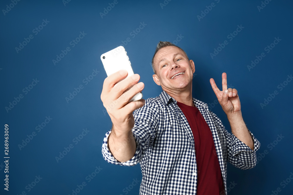Happy middle-aged man taking selfie on color background