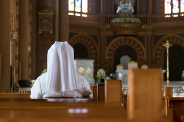 The nun sits in the church and prays to God. A nun in traditional white robes meditates in a Christian cathedral. Prayer to Jesus.