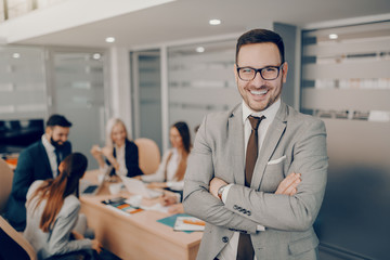 Handsome smiling businessman in formal wear and eyeglasses standing at boardroom with arms crossed. Love and respect do not automatically accompany a position of leadership. They must be earned