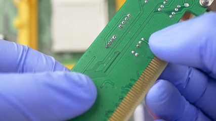 Hand in blue gloves holds contact system on PCI Express card for computer on electronic circuit motherboard background