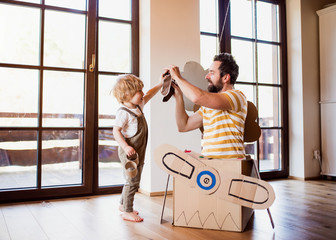 Wall Mural - A toddler boy and father with carton plane playing indoors at home, flying concept.