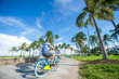 Tourists ride bicycles along the beachfront promenade in Lummus Park adjacent to historic Ocean Drive in South Beach, Miami, Florida, USA