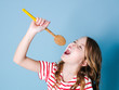 pretty cool and young girl uses cooking spoon as microphone and sings in front of blue background and is having a lot of fun