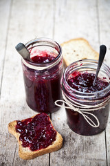 Cereal bread toasts slices and jars with homemade wild berries and cherry jam and spoons closeup on rustic wooden table background.