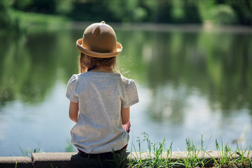 Girl sitting by the lake in the park back view