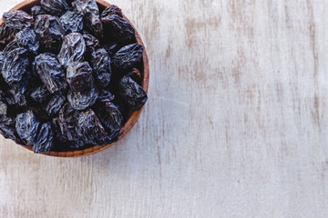 Sticker - Dark blue raisins in a wooden bowl on a bright white background. Close-up. Insulated.