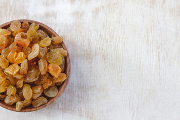 Sticker - Light yellow raisins in a wooden bowl on a light white background. Close-up. Isolated.