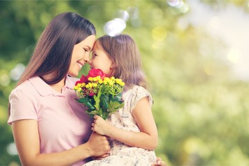 Wall Mural - Portrait of happy mother and daughter holding  flowers on natural background