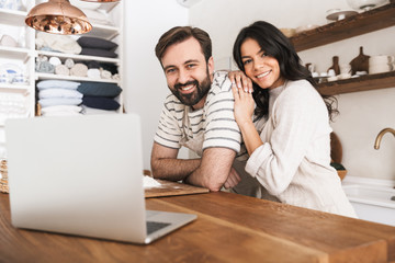 Sticker - Portrait of happy couple looking at laptop while cooking pastry in kitchen at home