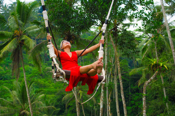 Wall Mural - attractive happy middle aged 40s or 50s Asian Indonesian woman with grey hair riding rainforest swing carefree swinging and enjoying tropical jungle adventure