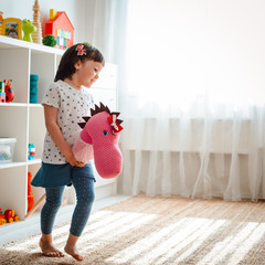 Wall Mural - little girl jumps and runs on a horse stick in the nursery.