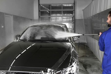 Canvas Print - Worker cleaning automobile with high pressure water jet at car wash