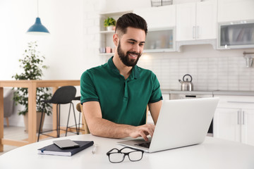 Wall Mural - Handsome young man working with laptop at table in kitchen