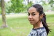 © Mangostar - Smiling pretty young woman posing at camera in park. Lady wearing sweater and looking at camera with green lawn and trees in background. Leisure and nature concept.