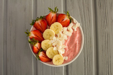 Wall Mural - Smoothies bowl with strawberries,banana and coconut chips on the grey wooden background.Top view.
