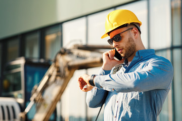 Construction engineer talking on the phone and looking at the watch on the construction site