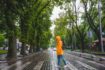 man crossing street in yellow raincoat. overcast weather