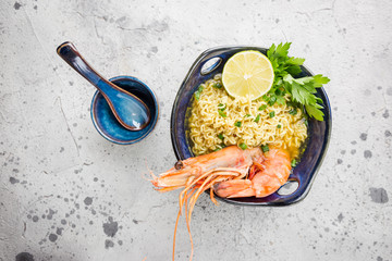 Wall Mural - A bowl of instant Chinese noodles with green onions, red hot chilli peppers, and shrimps on a gray stone background, top view