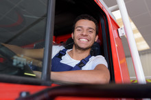 Portrait Of Happy Young Fireman Driving Firetruck At Station