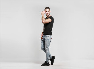 Poster - Muscular model sports young man in jeans and black t-shirt on a grey background. Fashion portrait of brutal sporty healthy strong muscle guy with a modern trendy hairstyle.