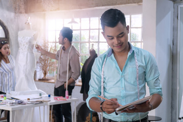 Creative designer young man standing with designer team working in the studio. Fashion male holding book and pen in his hand with professional design group working in their studio. Teamwork concept.