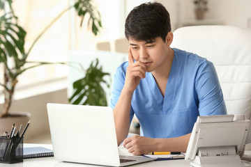 male medical assistant working on laptop in clinic