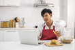 © mrwinn - Asian man in white shirt and red apron in a white kitchen holding french fried and using a laptop