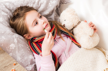 Little ill girl with bear measuring temperature