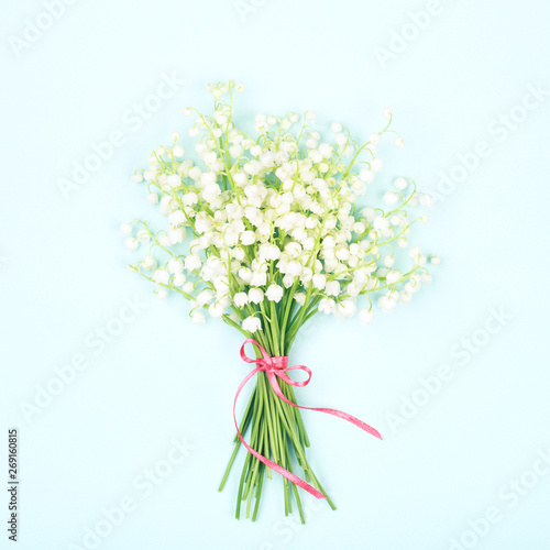 Bouquet of lily of valley tied pink ribbon on blue background. Tender spring ...