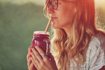 Wall Mural - Beautiful woman using cellphone while drinking smoothie outdoors.