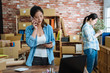© PR Image Factory - Woman online seller confirming orders from customer on mobile phone call. female ecommerce business owner looking at digital pad computer and talking on cellphone in store warehouse. colleague work