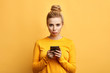 angry sad woman with hairbun annoyed by something while using phone, girl has received bad sms, text message isolated yellow background. emotion, reaction, feeling