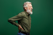 angry shouting old man suffering from back pain isolated on green background. close up side view photo. helath problem, senior man holding his back, having pain in kidneis.