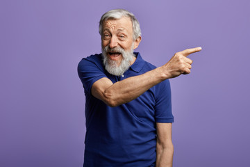 cheerful man pointing at copy space and looking at the camera. close up portrait, place for advert. happy old man indicating somewhere