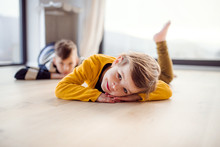 Two Happy Children Lying On Floor Indoors At Home.