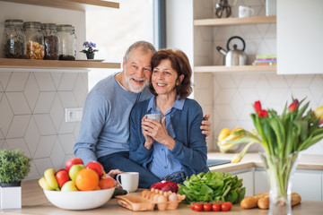 Wall Mural - A portrait of senior couple in love indoors at home, holding coffee.