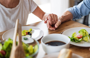 Wall Mural - A midsection of senior couple in love indoors at home, having lunch.