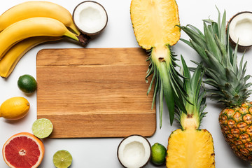 Wall Mural - top view of exotic fruits around wooden chopping board with copy space on white background