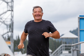 Smiling senior man running towards camera in rainy weather