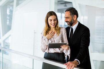 Handsome smiling mature businessman and his cute young female coworker with digital tablet in the office