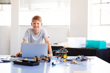 portrait of male student building and programing robot vehicle in school computer coding class