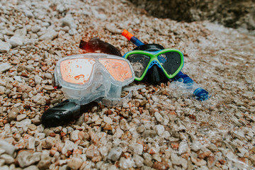 Snorkelling masks on pebble beach. Two diving masks and snorkels with drops of water washed by sea waves.