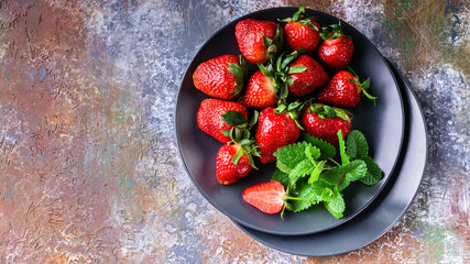 Juicy strawberries and mint on a shade plate on a rusty background. Top view