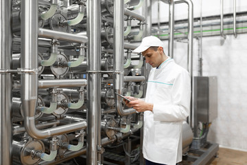 Wall Mural - Portrait of man in a white robe and a cap standing in production department of dairy factory with grey tablet