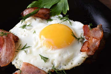 Morning breakfast with fried eggs with slightly fried bacon and parsley on a balck plate.