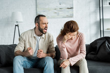 Angry Man Sitting On Sofa And Screaming At Upset Woman
